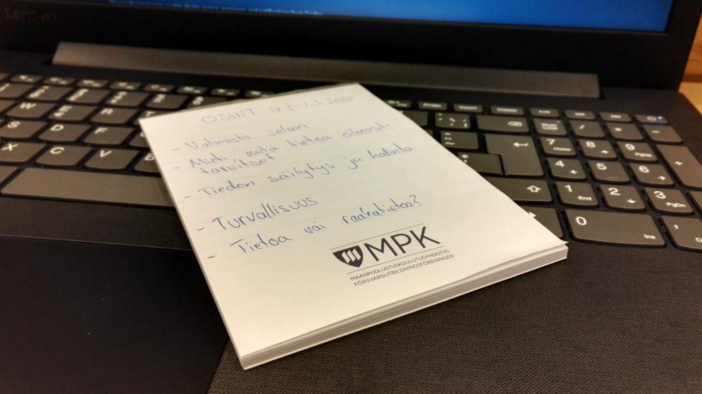 Kuva lehtiöstä jossa muistiinpanoja kannettavan tietokoneen päällä.