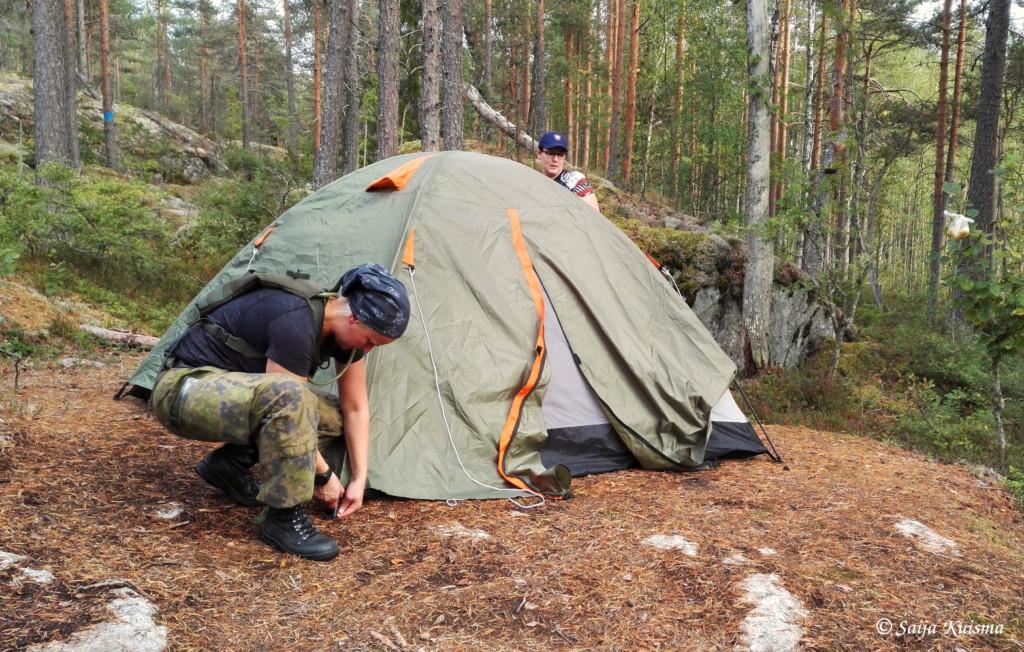 Kuva naisista, jotka pystyttävät retkitelttaa metsässä.