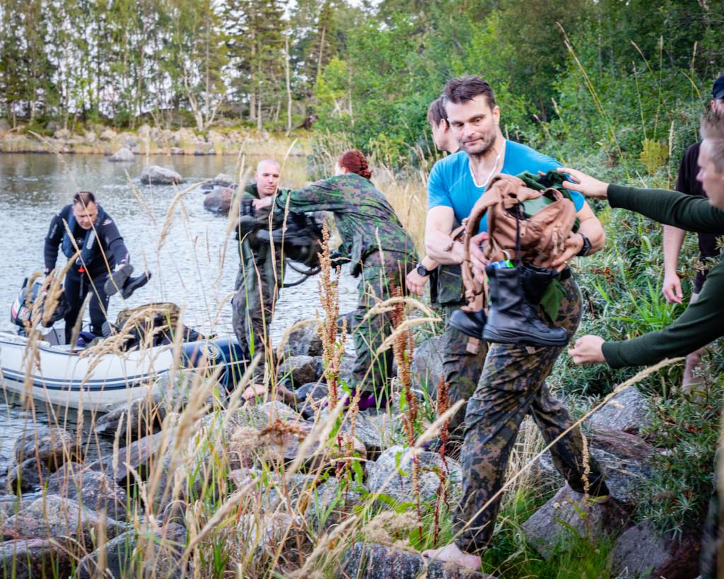 Joukko ihmisiä nostelee letkassa varusteita veneestä