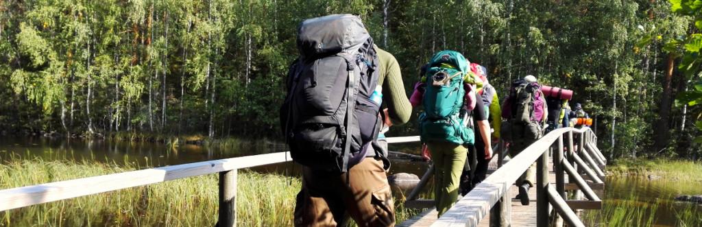Maastotaitokurssilaiset vaeltavat rinkka selässä puisen sillan yli.