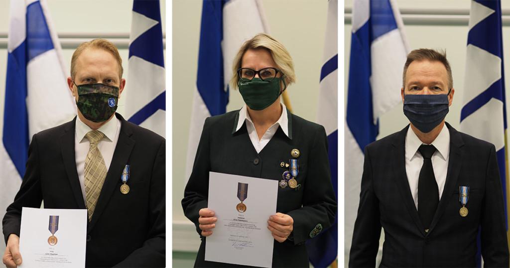 Maanpuolustusmitalien saajat seisovat kunniakirjojen kanssa maskit kasvoilla