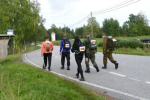 Viisi marssijaa kävelee asvaltilla.