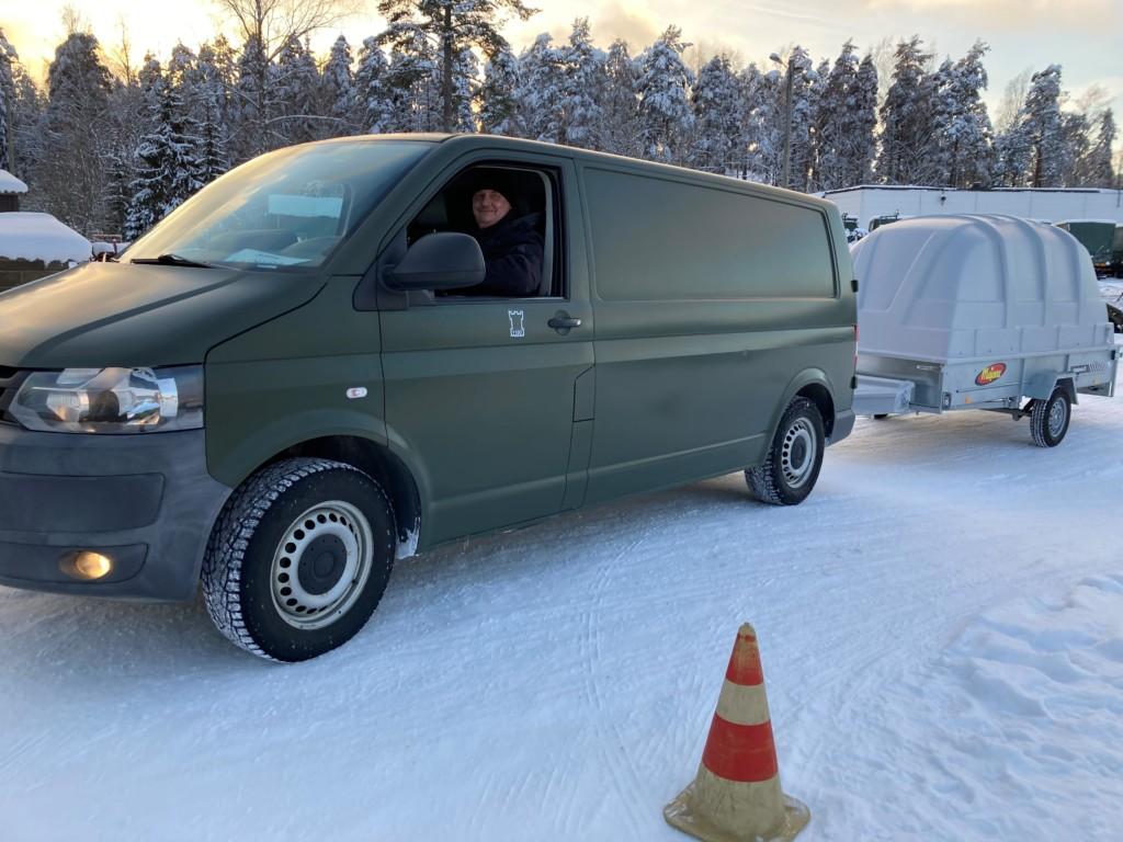 Mies ajaa pakettiautoa peräkärryn kanssa