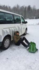 Mies pitää taukoa maassa istuen autoon nojaten
