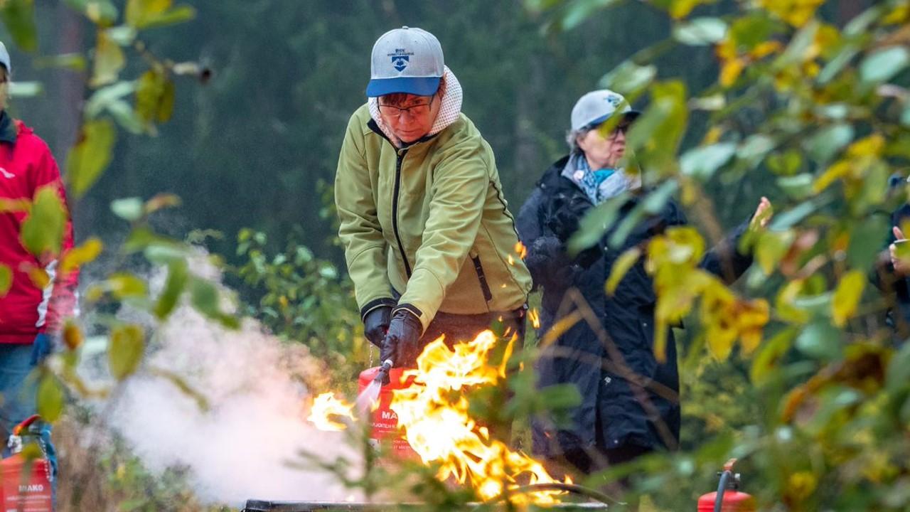 Nainen sammuttaa tulta vaahtosammuttimella vihreässä, metsäisessä ympäristössä.