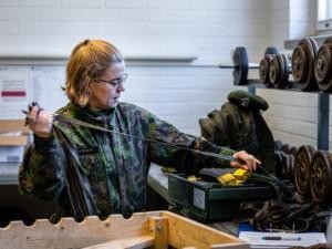 Nainen maastopuvussa ottaa kengännauhoja käteensä