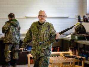 Mies maastopuvussa ase molemmissa käsissä asevarastolla