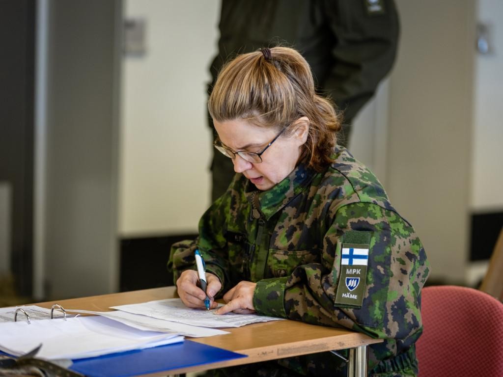 Nainen pöydän ääressä kirjoittaa paperille