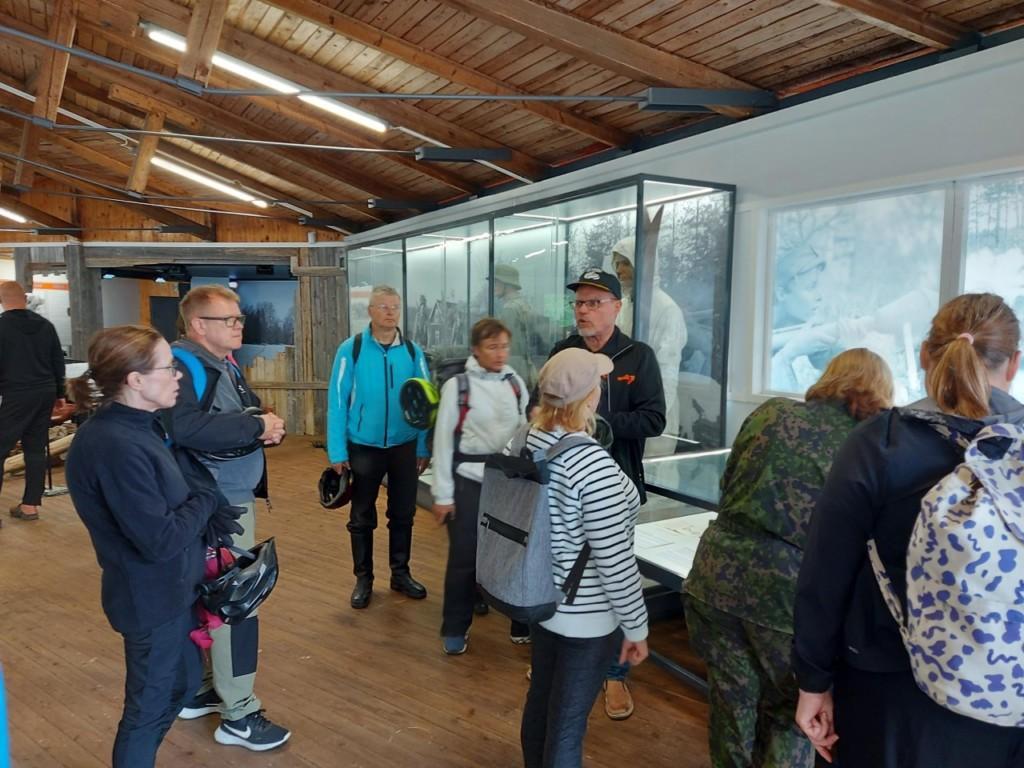 Ihmiset panssarimuseolla kuuntelemassa oppaan esitystä