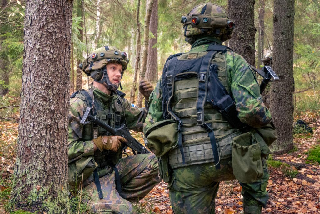 Kaksi reserviläistä polviasennossa taisteluvarustuksessa metsässä.