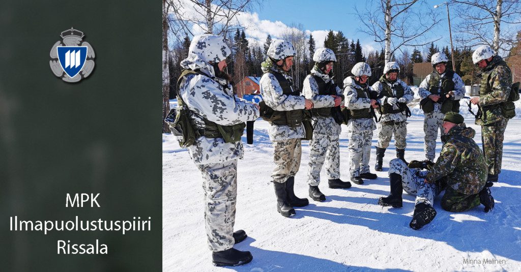 Ilmapuolustuspiirin talvinen koostekuva taistelijan ensiavun opetustilanteesta, osallistujat lumipuvuissa ja kouluttajat puolustusvoimain vaatteissa.