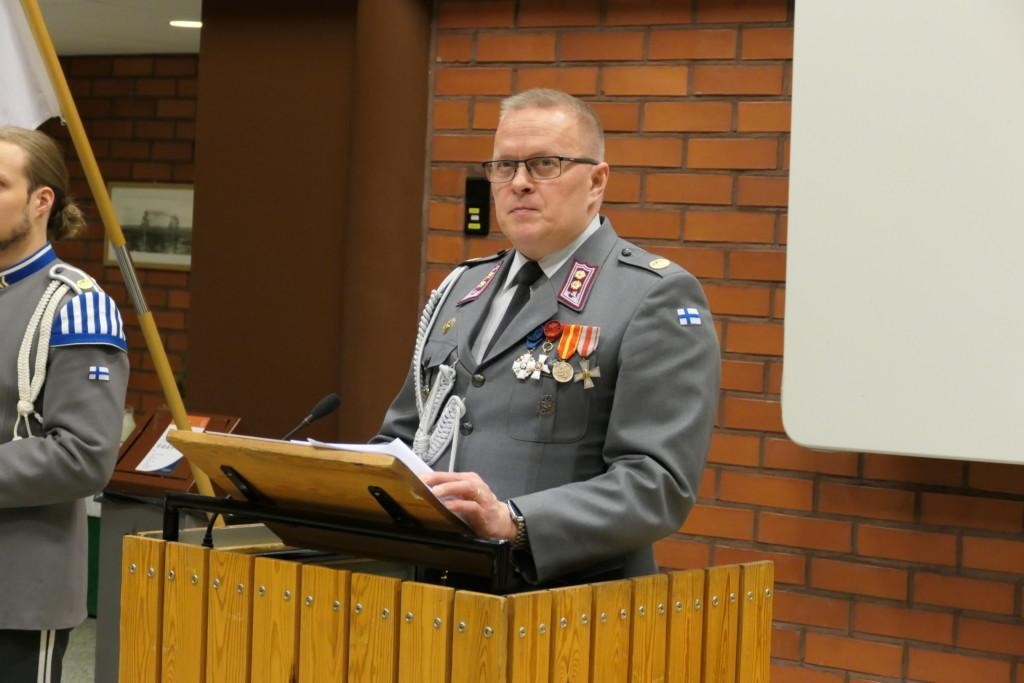 Mies sotilasasussa pitää juhlapuhetta