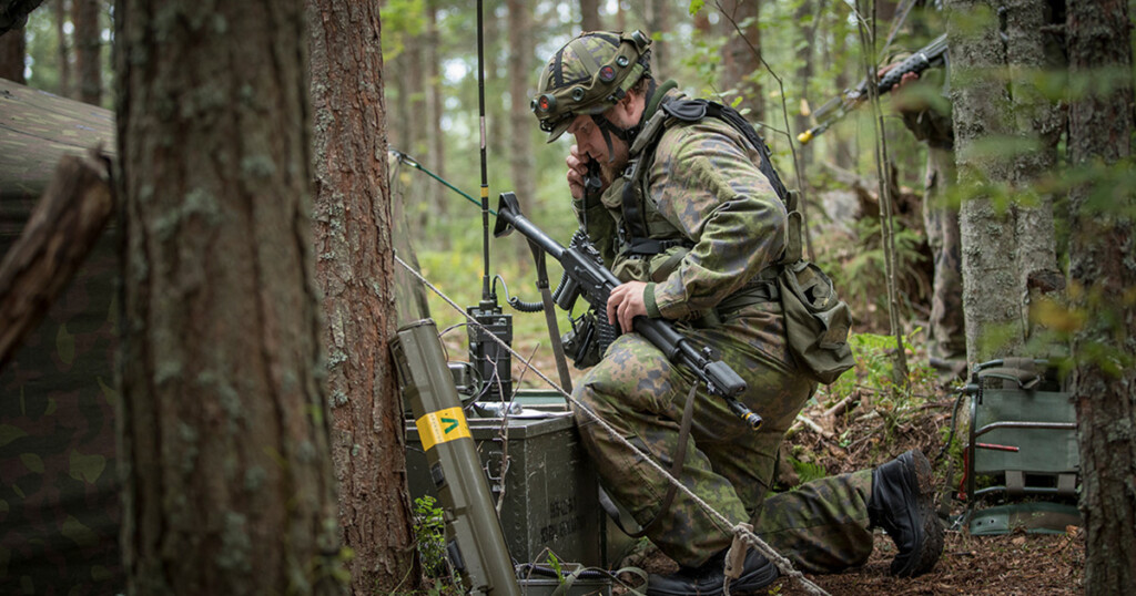 Maastoasuinen henkilö puhuu kenttäradioon metsässä.