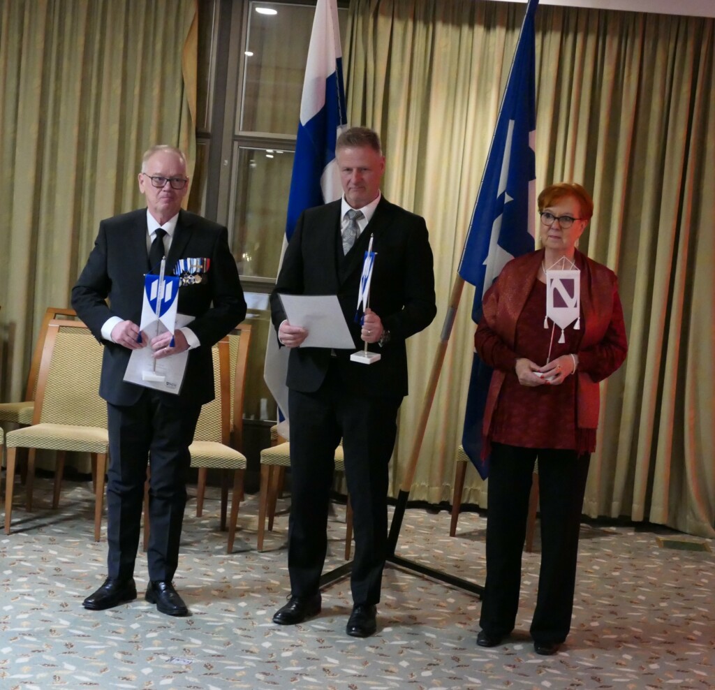 Palkittavat, kaksi miestä ja yksi nainen standaarit kädessä