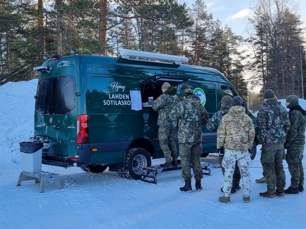 Sotilaskotiauto, johon ihmisiä jonossa ostoksille