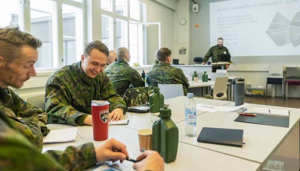 Maastoasuisia henkilöitä luokassa seuraamassa luentoa