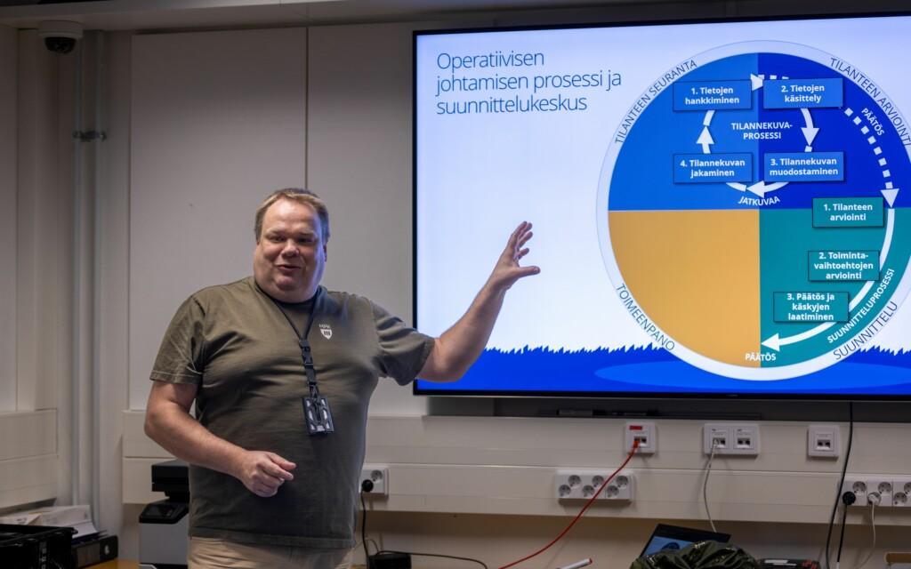 Mies puhuu edessä ja takana näkyy PowerPoint esitys