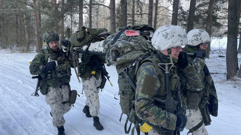 Neljä maastopukuista henkilöä kantaa potilasta paareilla.