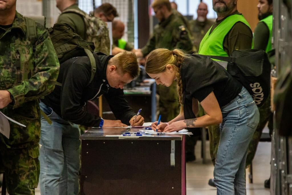 Nainen ja mies pöydän ääressä seisten kirjoittamassa paperille