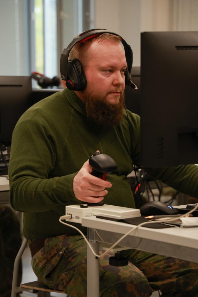 Vihreäpaitainen parrakas mies istuu tietokoneen ääressä kuulokkeet päässään.