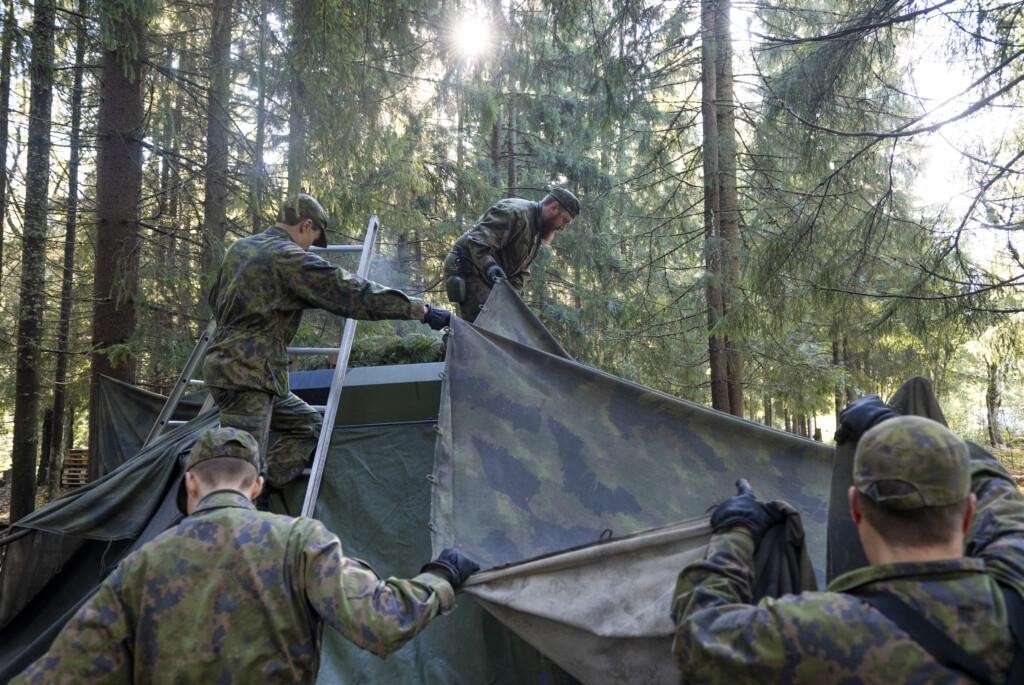 Neljä sotilasta asettaa naamioverkkoa tikkaiden avulla.