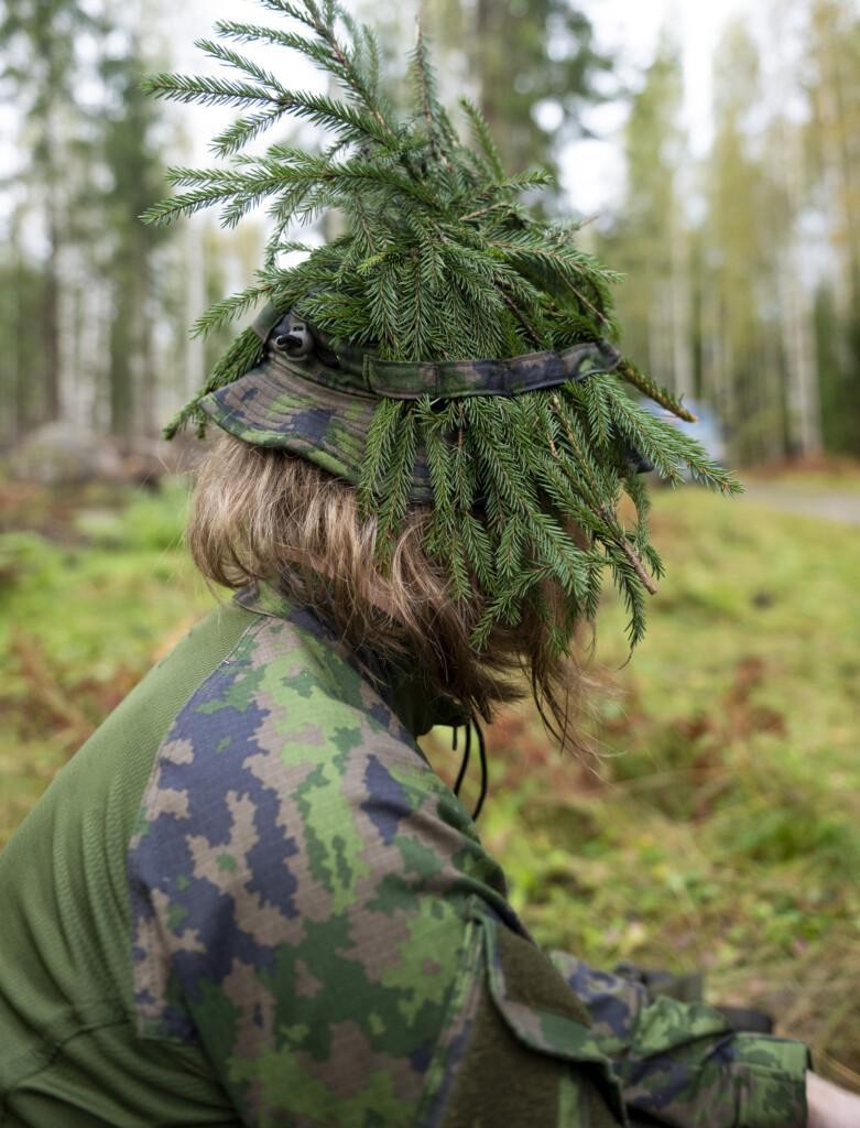 Sivuprofiili sotilaasta, jolla on havuja lierihatussa.
