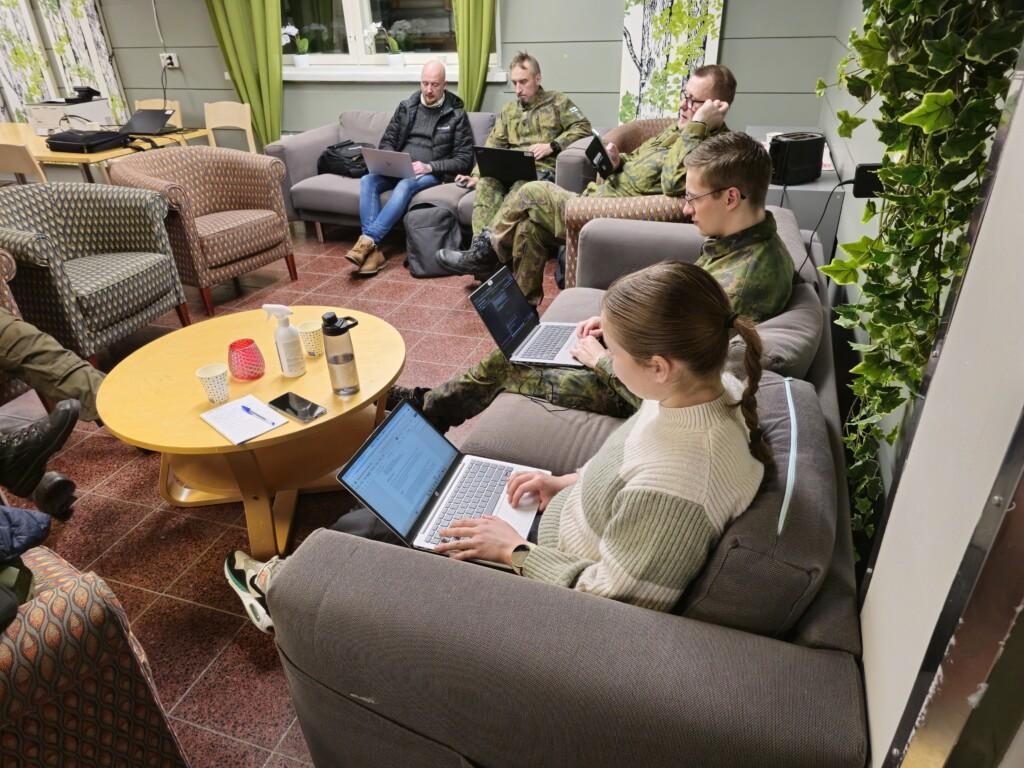 Viisi henkilöä työskentelemässä kannettavien tietokoneiden kanssa sohvaryhmällä, kukin omalla sohvallaan.