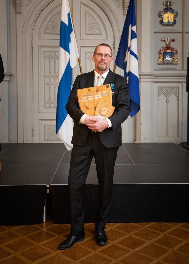 Mies seisoo lippujen edessä puukilpi sylissään