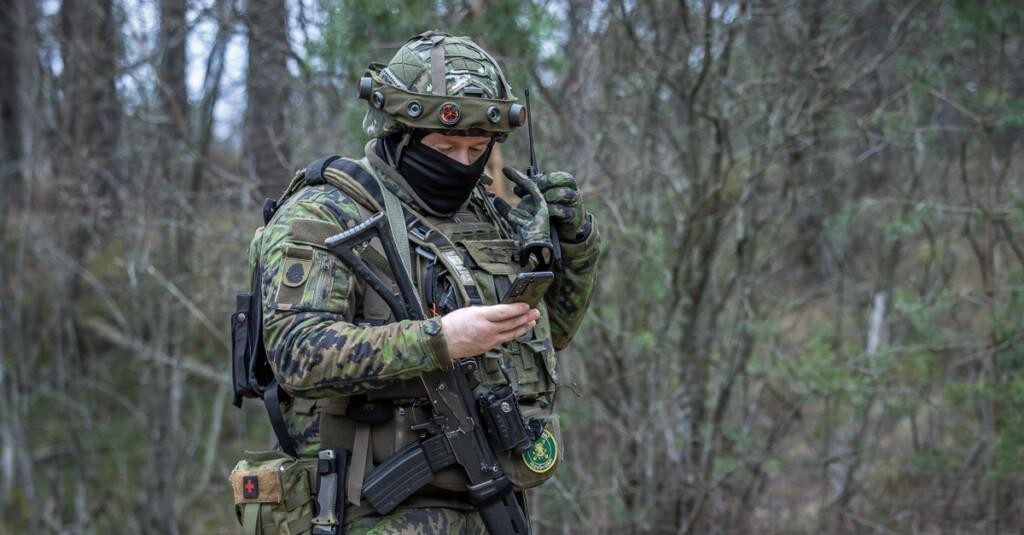 Maastopukuinen henkilö katsoo kädessään olevaa kännykkää.