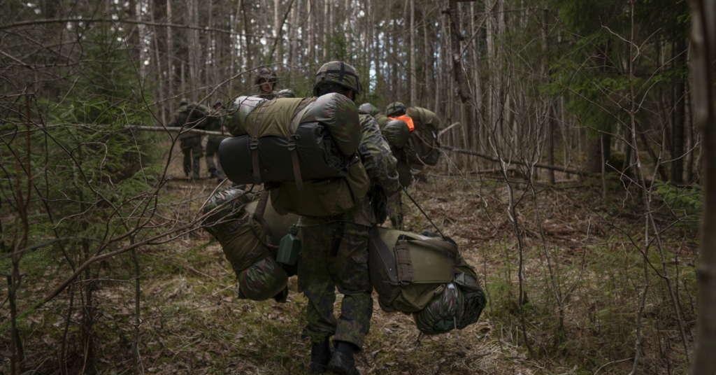 Reserviläisiä kävelemässä metsässä kantaen reppuja ja muita varusteita.
