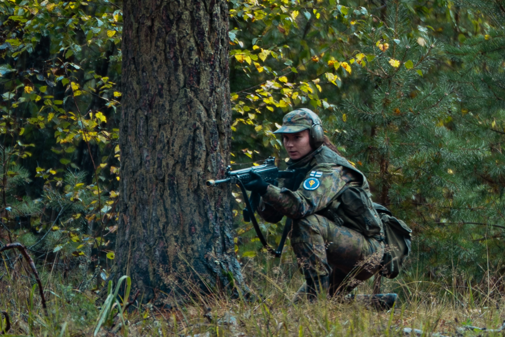 Nainen metsässä kivääri kädessä kohdetta suojaamassa